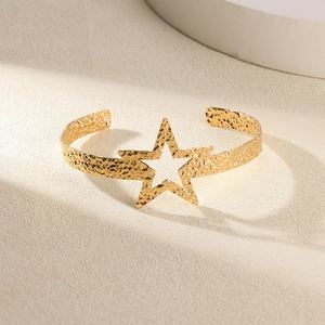 Détail d'un bracelet manchette doré martelé avec découpe étoile sur fond minimaliste