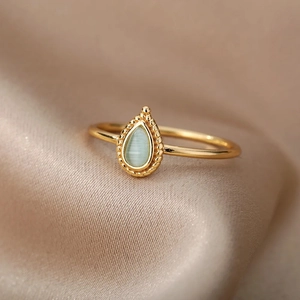 Macro detail of a gold ring with a pear-shaped opal on luxury silk background