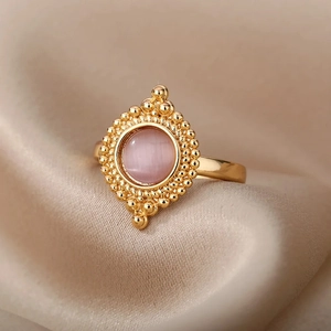 Macro view of a gold oval ring featuring a pink cat eye stone on champagne satin
