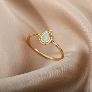 Macro detail of gold oval gemstone ring with bead trim on a champagne silk background