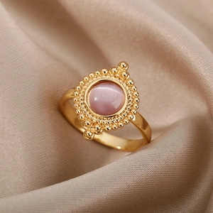 Detailed view of vintage gold ring with pink opal stone and milgrain edging on silk