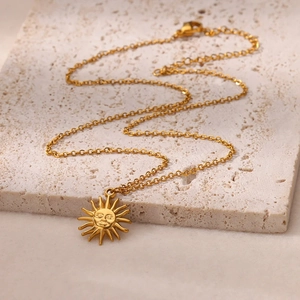Elegante collana con ciondolo a sole dorato esposta su una base di pietra travertino