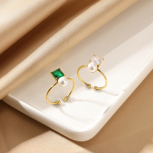 Detail view of open gold rings with square zircon and emerald gemstone and pearls