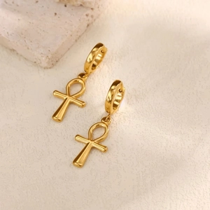 Detail von vergoldeten Ankh-Symbol-Ohrhängern auf minimalistisch strukturiertem Grund