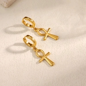 Polierte goldene Ankh-Kreuz-Ohrhänger auf einem strukturierten Steinhintergrund