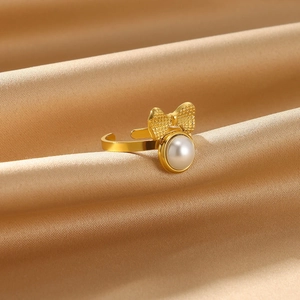 Detail of gold open ring with bow design and white pearl on champagne silk fabric