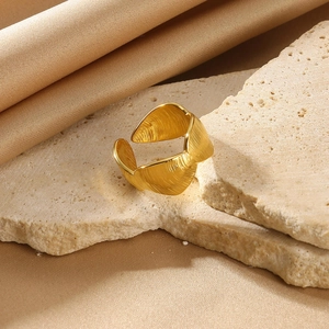 Detail of gold-plated open ring featuring leaf-shaped components and brushed metal texture