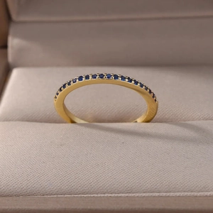Golden ring with micro-paved blue zircons displayed in a beige jewelry gift box