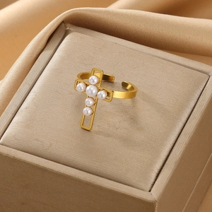 Detail of a gold adjustable ring featuring a pearl-inlaid cross on silk fabric