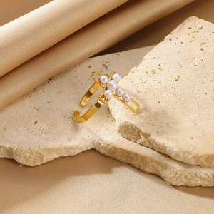 Detail of a gold-plated cross ring with six white pearls on a minimalist background