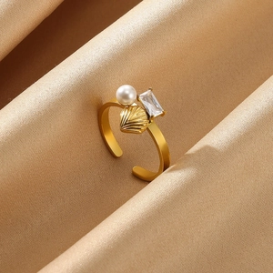 Close-up of a gold ring with a white pearl, shell design, and rectangular zircon detail