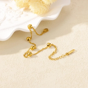 Close-up of 18k gold plated bracelet with wave chain and five gold beads on a ceramic plate