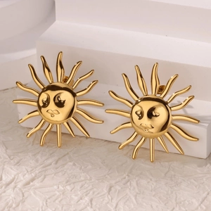 Detailed view of gold plated sun earrings with facial features on a white display stand