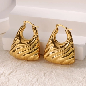 Detail shot of chunky gold-plated hoop earrings with textured wave patterns and latch back