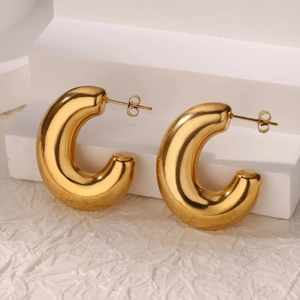 Macro view of polished gold-plated thick C-shaped hoop earrings on a white stand
