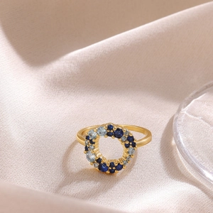 Macro view of 18K gold bow ring with blue zircon stones on textured beige fabric