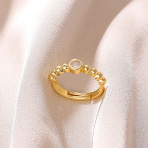 Detail of 18K gold plated beaded ring with a sparkling zircon on pink fabric