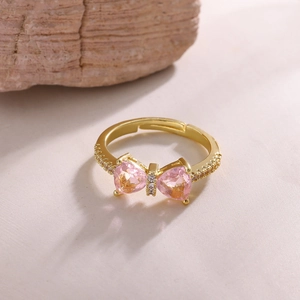 Macro detail of 18K gold bow ring featuring heart-shaped pink zircons and small white diamonds