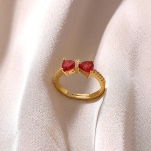 Detail of 18K gold plated bow ring with red triangle stones on white silk fabric