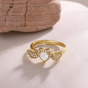 Detail of 18K gold plated heart ring with angel wings and zircon inlay on stone surface