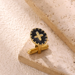 Luxurious gold oval cufflink with black enamel and cross star on beige stone background