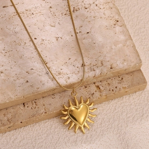 Collier soleil en acier inoxydable doré avec pendentif cœur sur fond de pierre travertin