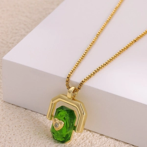 Detail view of gold necklace featuring green gemstone pendant with zircon heart inlay