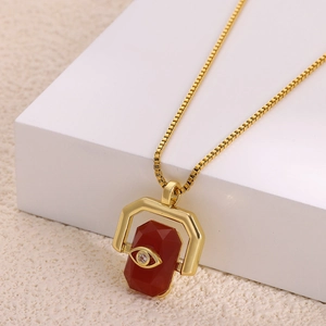 Detail of gold necklace showing evil eye pendant with red stone on white props