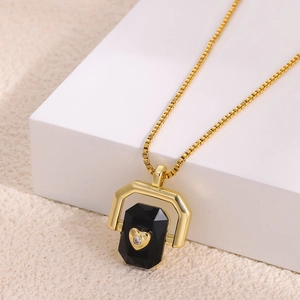 Close-up of golden necklace featuring a black hexagonal stone with a diamond heart inlay