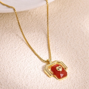 Detail of gold box chain necklace with red gemstone pendant and heart crystal inlay