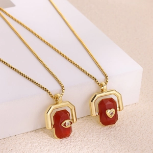 Golden box chain necklace with rotating red stone pendants featuring evil eye and heart charms