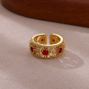 Detalle de anillo vintage dorado con diseño calado, piedras rojas y circonitas