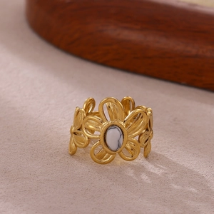 Detalle de anillo de flor chapado en oro con piedra de turquesa blanca central