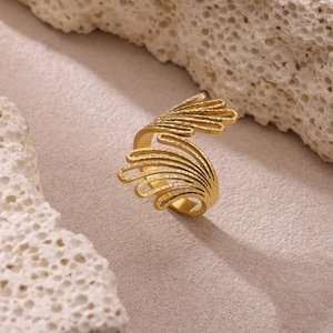 Anillo vintage de capas con alas huecas doradas y perlas sobre fondo de piedra coral