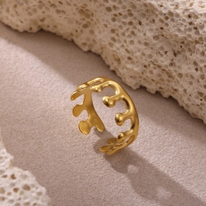 Anillo artístico de ondas doradas con estética fluida sobre fondo de piedra coral