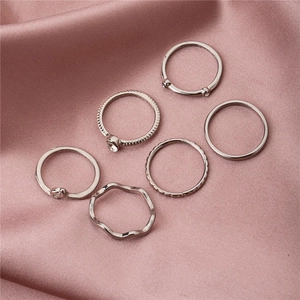 Elegantes Set aus sechs silbernen Ringen mit Strass und Textur auf rosa Seidenstoff