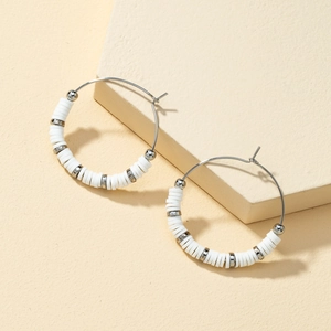 Detailed view of silver hoop earrings with white clay beads on a beige pedestal