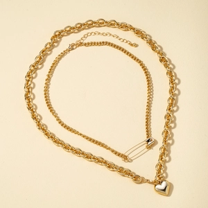 Detailed view of layered gold heart necklace with safety pin pendant and cable chain link