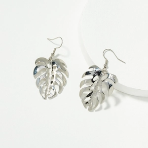 Boucles d'oreilles feuille de monstera en argent sur un présentoir blanc minimaliste