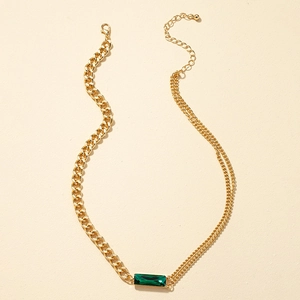 Detail einer goldfarbenen asymmetrischen Halskette mit smaragdgrünem Stein und Cuban-Gliedern