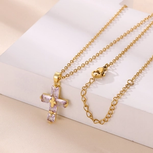 Collana con ciondolo a croce dorata e pietre viola su un supporto geometrico bianco