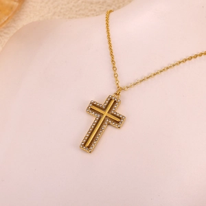 Dettaglio del ciondolo a croce dorata con zirconi luccicanti su collana a maglia O