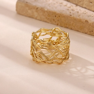 Detailed view of a wide gold-plated stainless steel woven ring on a textured surface