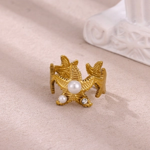 Detail of gold starfish ring featuring white pearls and zircon on a textured surface