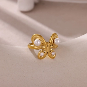 Detail of matte gold butterfly ring featuring white pearls on beige ceramic background