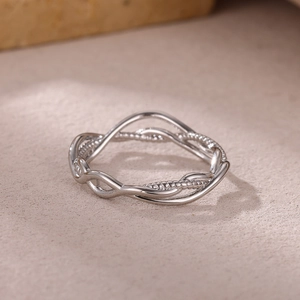 Macro shot of silver wave ring featuring twisted woven design on a textured beige surface