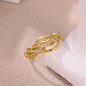 Macro detail of gold wavy intertwined ring with bead accents on white stone