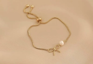 Detail of 18K gold plated box chain bracelet with woven bow and pearl charm accent