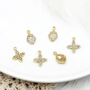 Macro detail of 18K gold plated strawberry and four-leaf clover charms with white zircons