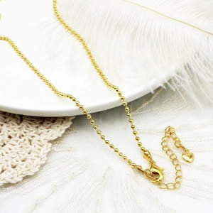 Detail van 18K vergulde kralenketting met karabijnsluiting en hartvormige bedel aan het einde